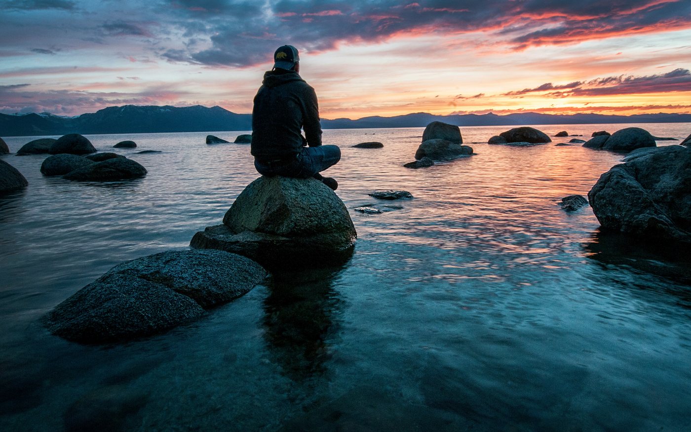 Person sitzt ruhig am Wasser im Abendlicht