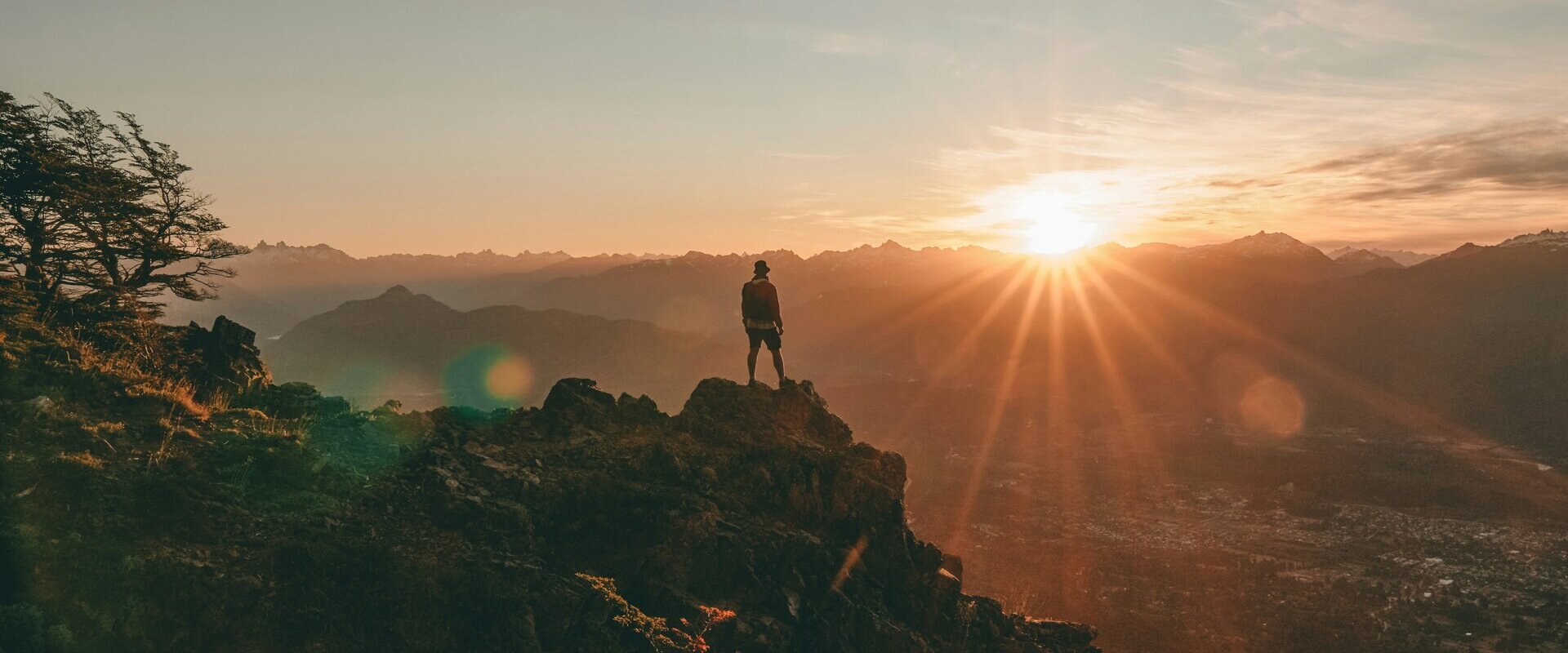 Ein Wanderer steht auf einem Bergkamm und blickt über ein weites Tal bei Sonnenaufgang