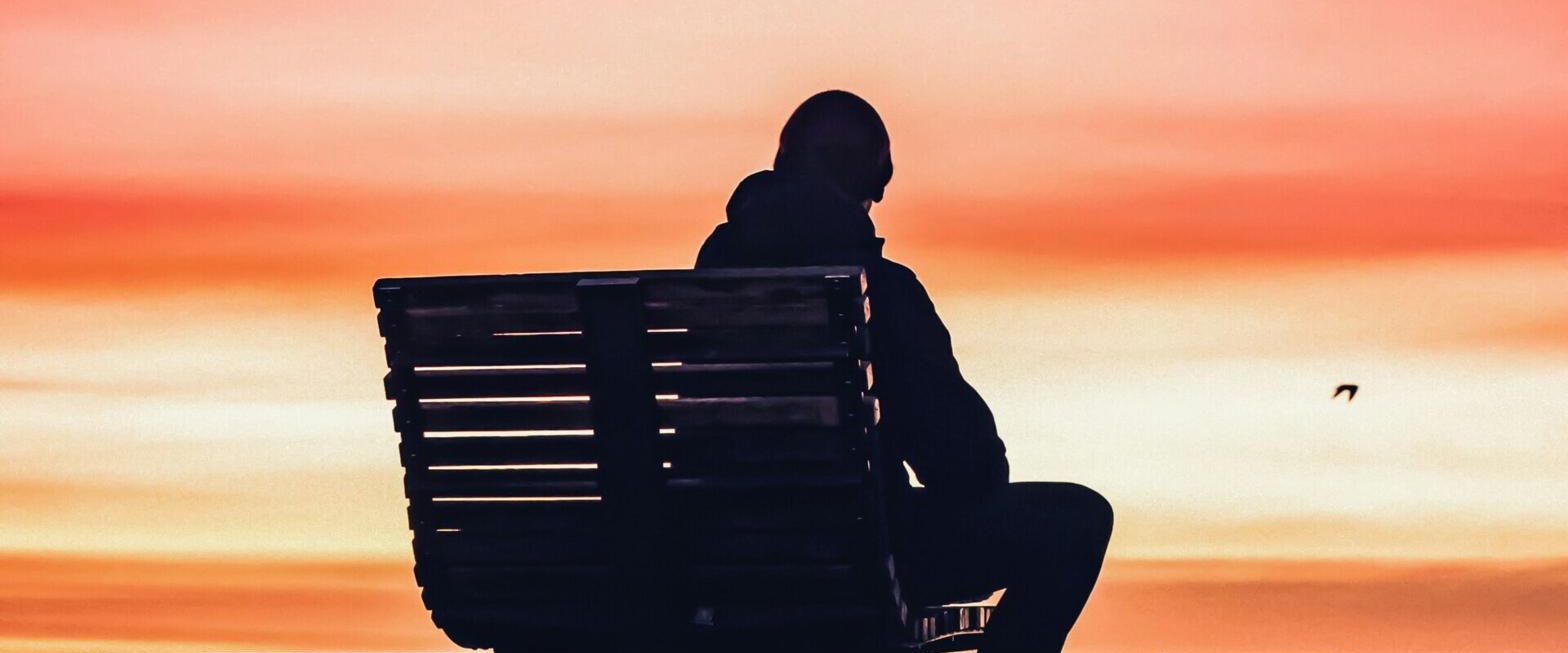 A person sitting alone on a bench at sunset